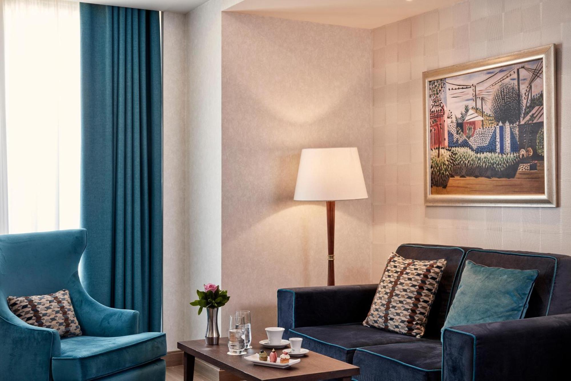 Electra Metropolis Hotel Athens Exterior photo The photo shows a stylish and modern living space. There is a dark blue couch adorned with decorative cushions, paired with a comfortable blue armchair. A coffee table in the center features a small floral arrangement and a couple of glassware items,
